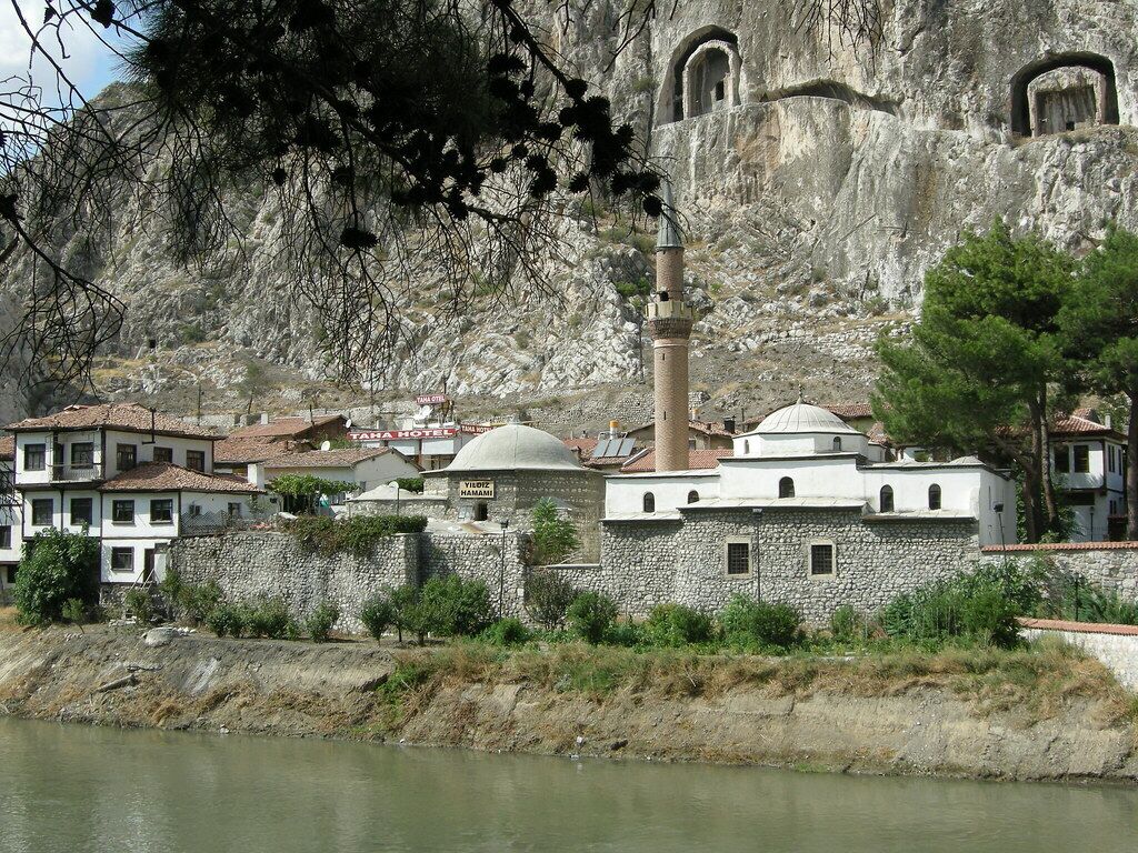A historic building with a minaret and a dome, surrounded by a stone wall and a river.