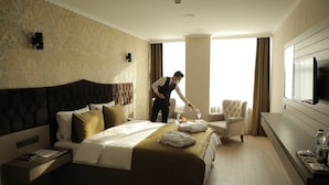 A hotel room with a large bed, a sitting area with a chair, a flat-screen TV, and a minibar. - ELİT OTELHAN (Amasya)