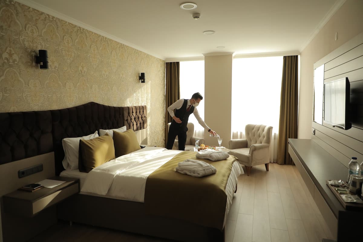 A hotel room with a large bed, a sitting area with a chair, a flat-screen TV, and a minibar.