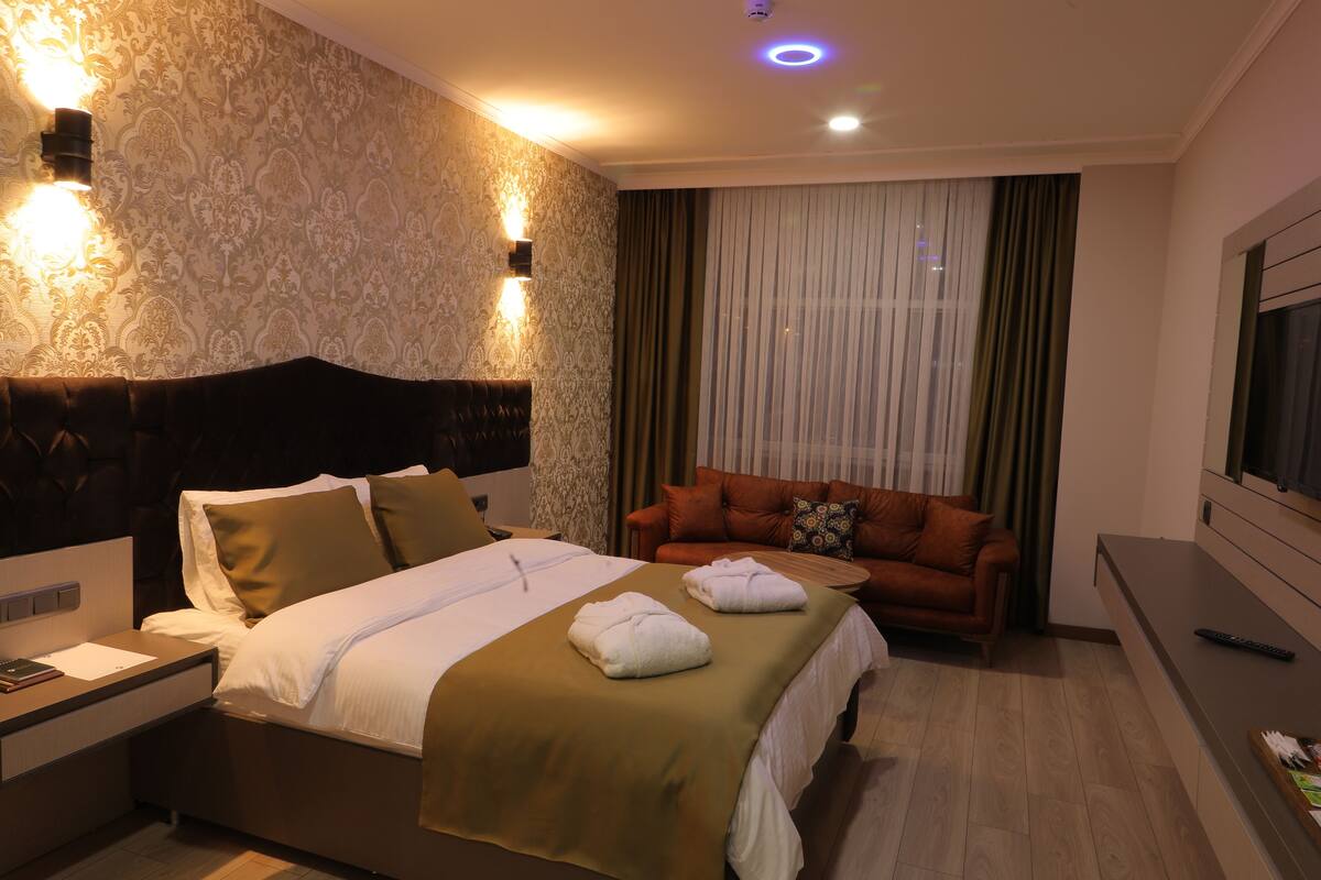 A hotel room with a large bed, a sofa, a nightstand, and a TV.