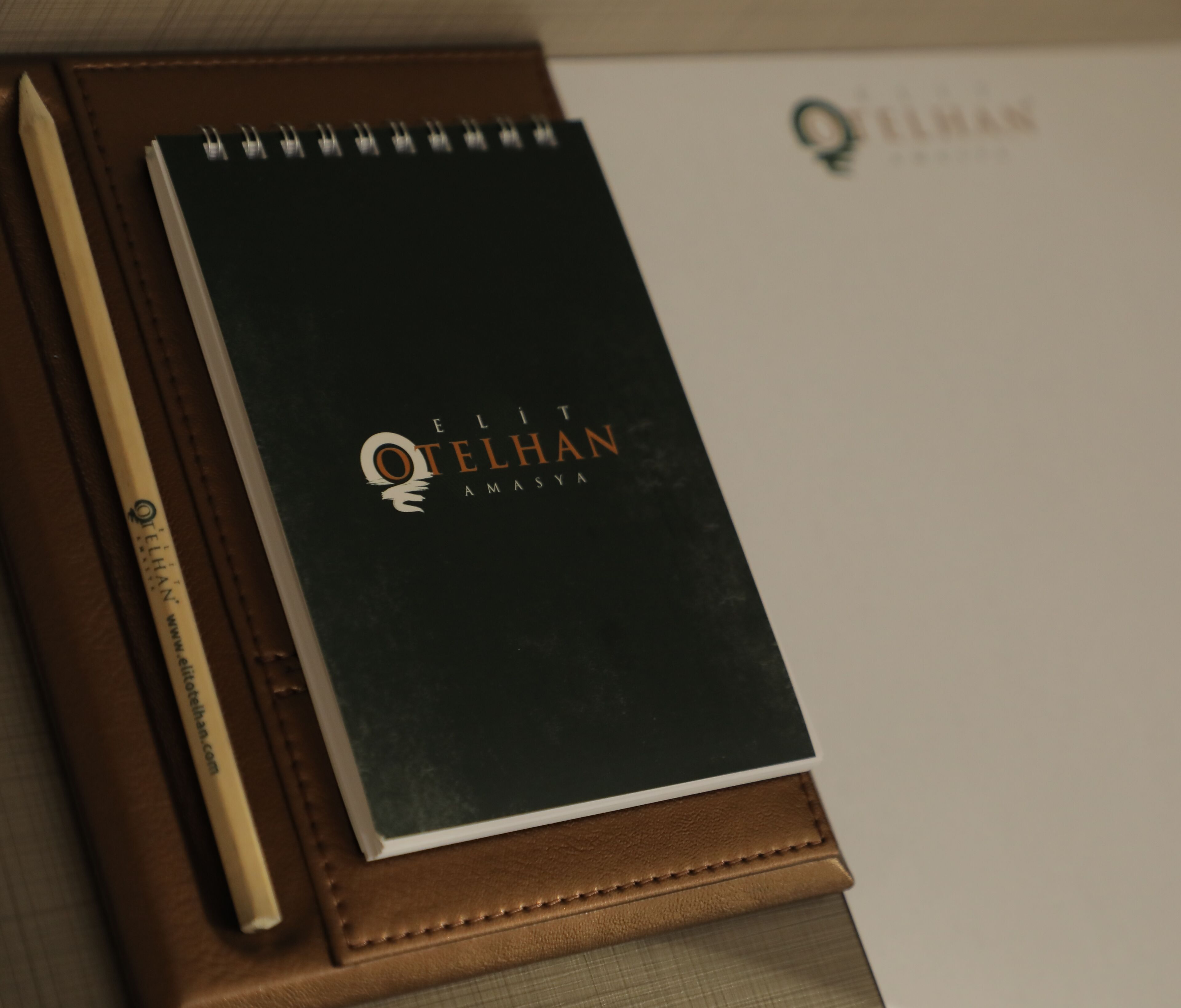 A notebook with the title "ELIT OTELHAN AMASYA" on its cover, placed on a brown leather case.