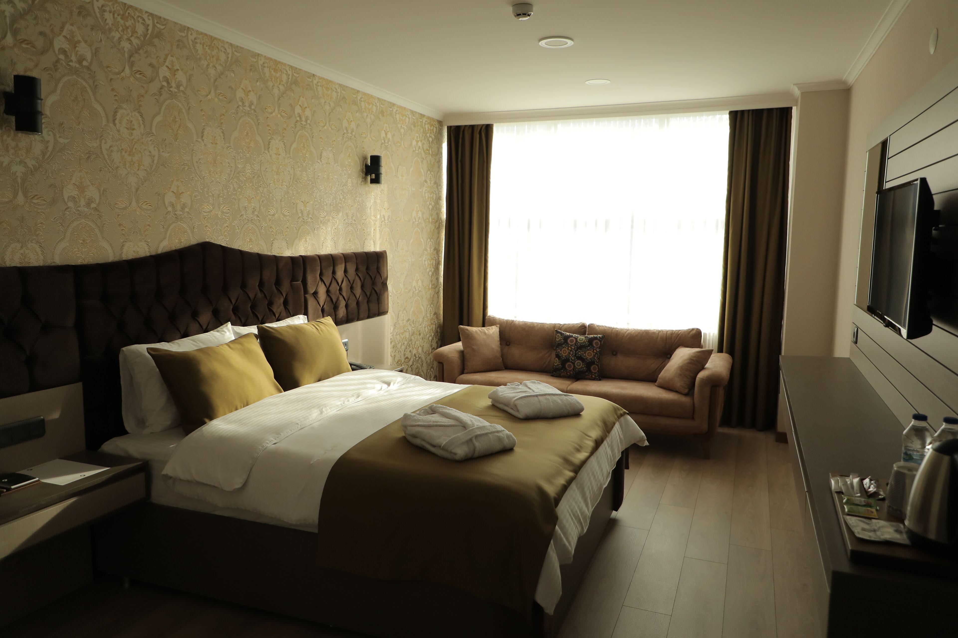 Ein Hotelzimmer mit einem großen Bett, einem Sofa, einem Fernseher und einem Schreibtisch mit Wasserkocher.