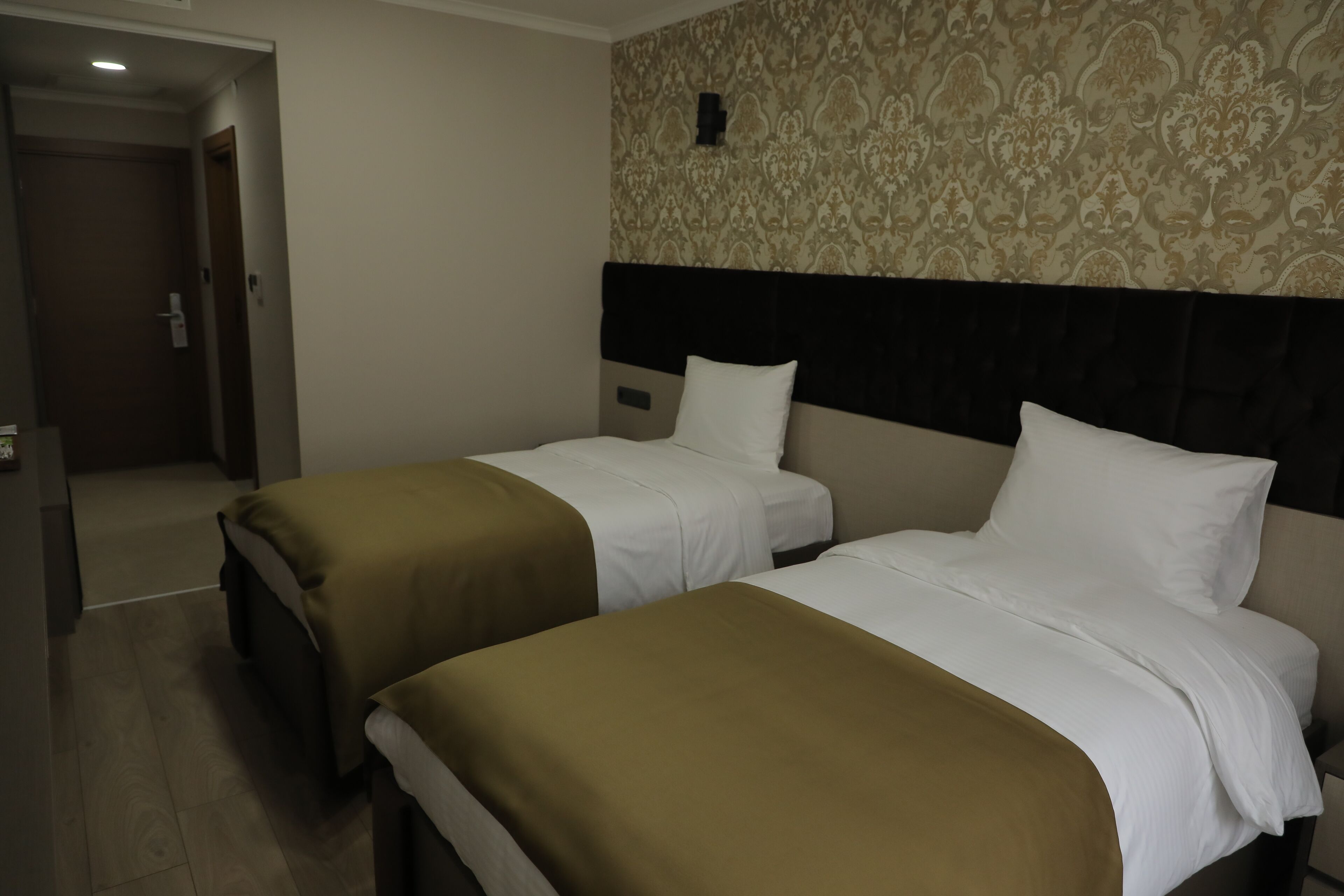 Una habitación de hotel con dos camas, un papel tapiz estampado y una puerta que da a otra habitación.