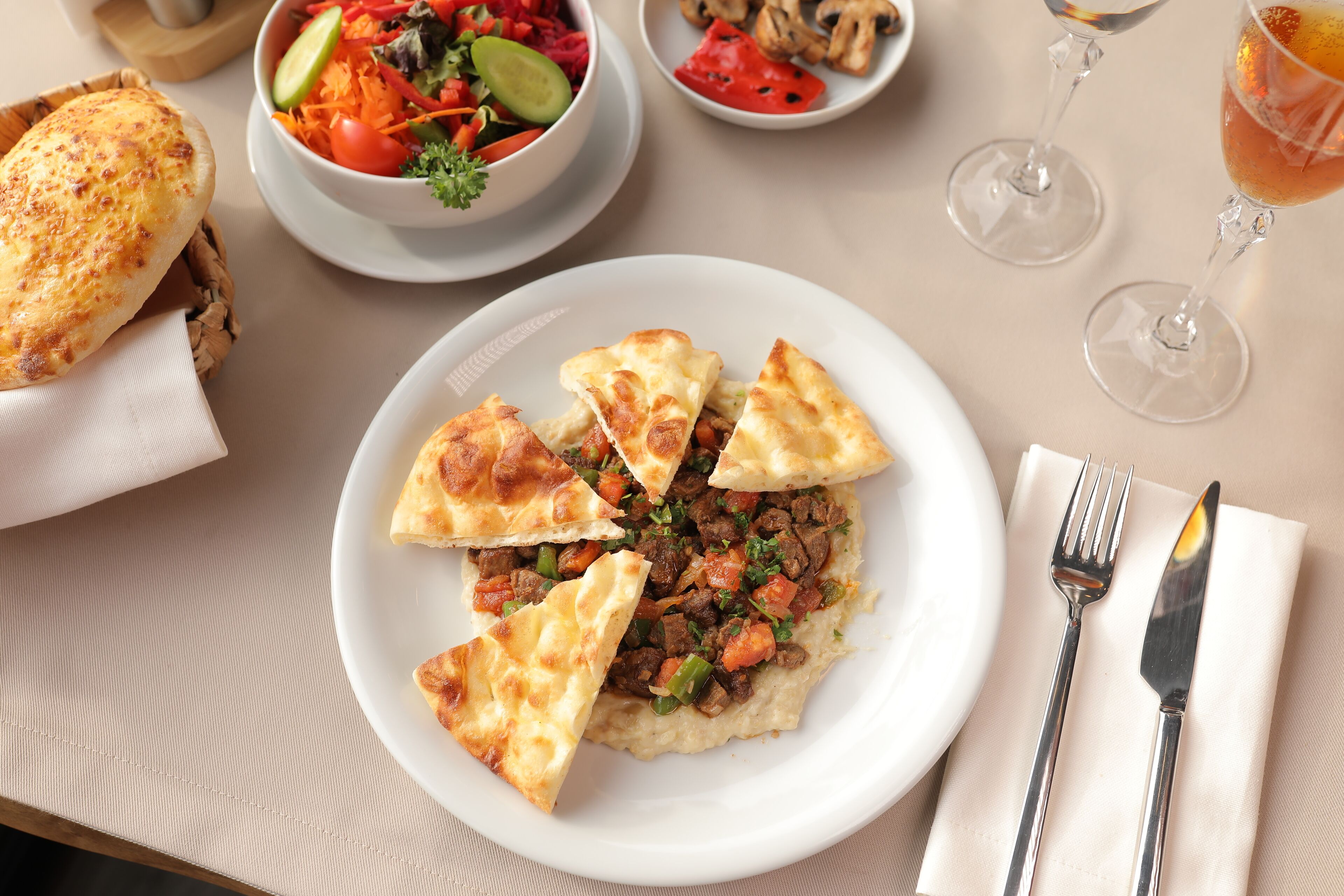 A table with a plate of food, a bowl of salad, a glass of drink, and cutlery.
