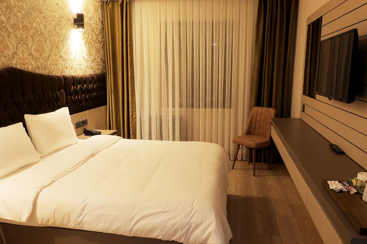 A hotel room with a large bed, a chair, a TV mounted on the wall, and a window with curtains.