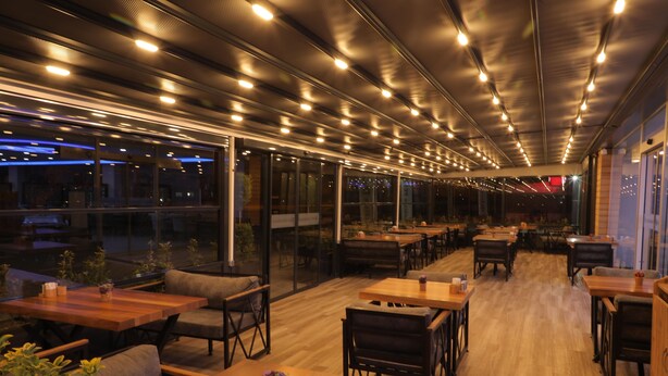 A modern restaurant with wooden tables and chairs, large windows, and a ceiling with multiple lights. - ELİT OTELHAN (Amasya)