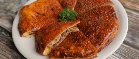 Um pastel redondo e dourado, coberto com sementes de sésamo, sobre um prato branco, decorado com salsa.