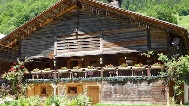 A rustic wooden building with a balcony, stone windows, and a mountainous backdrop.