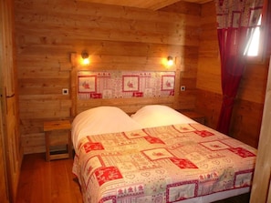 Une chambre dans une cabane en bois, avec un lit, une table de chevet et une tête de lit décorative.