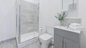 A modern bathroom with a glass shower enclosure, a toilet, and a vanity with a mirror. - Central Dudley 1BR Flat w/ Fast Wi-Fi (Dudley)