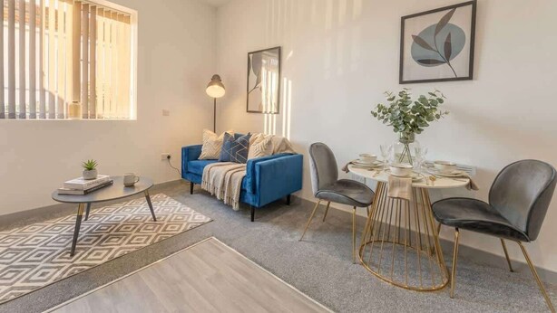 A modern living room with a blue sofa, a round dining table with chairs, a floor lamp, and a potted plant. - Central Dudley 1BR Flat w/ Fast Wi-Fi (Dudley)