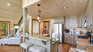 A spacious kitchen with wooden cabinets, a central island with bar stools, and a stainless steel refrigerator.