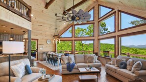 A spacious living area with a large wooden ceiling, multiple windows offering scenic views, and a dining area with a view.