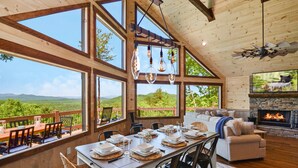 A dining area with a table set for six, large windows, a fireplace, and a view of the outdoors.