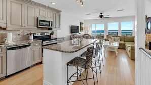 A spacious kitchen with a large island, a dining area with a view of the ocean, and a living room with a sofa and a TV. - Gulf View Townhome | Prime Beach Location, Walk to Multiple Restaurants! (Santa Rosa Beach)