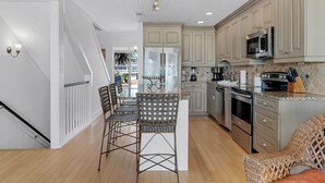 A modern kitchen with a central island, stainless steel appliances, and a dining area with wicker chairs. - Gulf View Townhome | Prime Beach Location, Walk to Multiple Restaurants! (Santa Rosa Beach)
