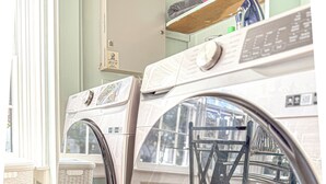 A laundry room with two front-loading washing machines, wooden flooring, and a chair visible through the glass door. - Groton Bay / Heated pool opens May 6th 2023! (Groton)