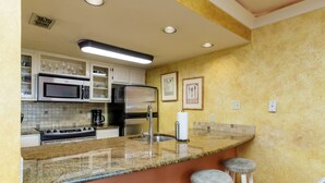 A kitchen with granite countertops, stainless steel appliances, white cabinets, and a yellow accent wall. - Beachside Cozy Condo | Tropical Pool & Coastal Comfort (Corpus Christi)