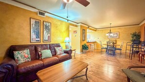 A living room with a brown leather sofa, a wooden coffee table, and a ceiling fan. - Beachside Cozy Condo | Tropical Pool & Coastal Comfort (Corpus Christi)
