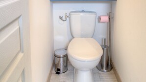 Une petite salle de bain comprenant des toilettes, une poubelle et un porte-rouleau de papier toilette.