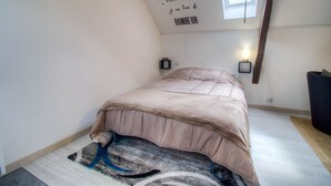 Une chambre à coucher avec un lit, une lampe fixée au mur, une petite étagère et une fenêtre.