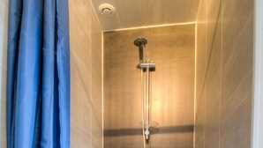 Une douche avec un rideau bleu, une douchette à main et un panneau de commande fixé au mur.