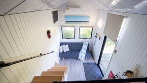 A compact room with a staircase, a sofa, and a window with a view. - Baxter at Lake George Winery by Tiny Away (Lake George)