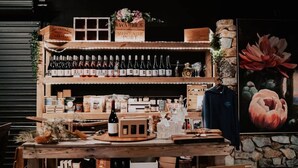 A wooden bar area with shelves of bottles, a vintage sign, and a flower arrangement. - Baxter at Lake George Winery by Tiny Away (Lake George)