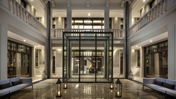 A spacious courtyard with a central glass door entrance, surrounded by seating areas and illuminated by lanterns.
