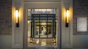A hotel entrance with a grand archway, a glass door, and two wall-mounted lights.