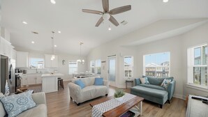 A spacious living area with a kitchen, a ceiling fan, and large windows.