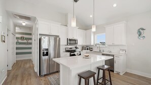 A modern kitchen with white cabinetry, stainless steel appliances, and a central island with stools.