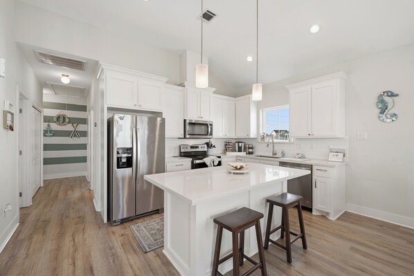 A modern kitchen with white cabinetry, stainless steel appliances, and a central island with stools.