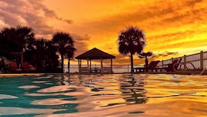 A swimming pool with a gazebo, palm trees, and a sunset.