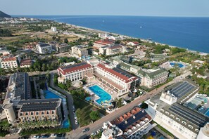 An aerial view of a coastal hotel complex with multiple buildings, a central swimming pool, and a view of the sea. - Hotel Camyuva Beach (Kemer)