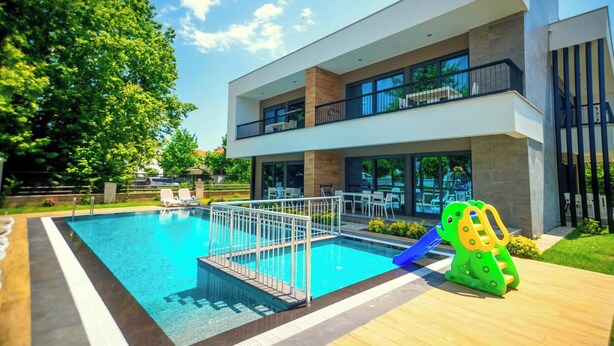 Un bâtiment moderne doté d’une piscine, d’un espace extérieur aménagé et d’une aire de jeux pour enfants.