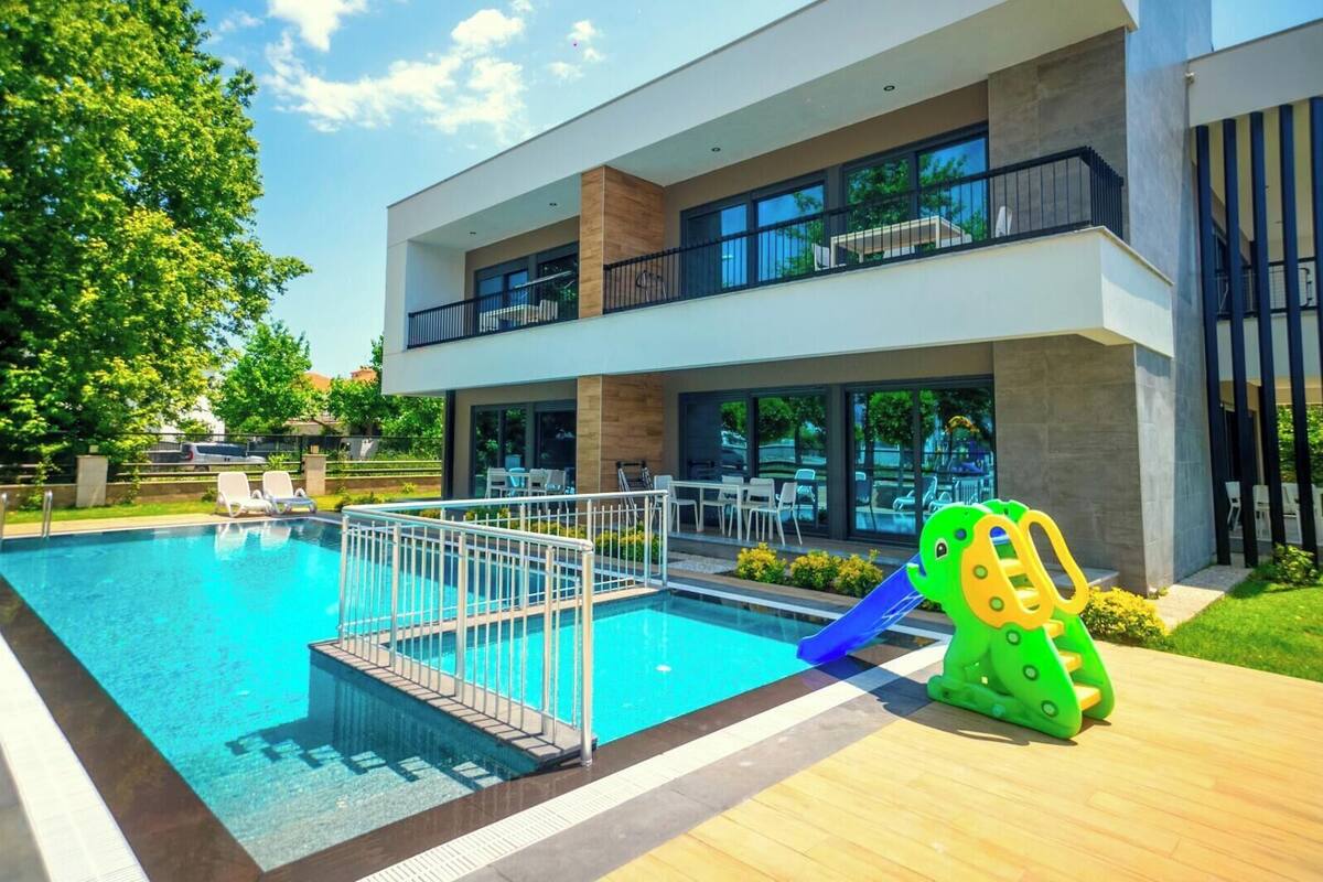 Un bâtiment moderne doté d’une piscine, d’un espace extérieur aménagé et d’une aire de jeux pour enfants.