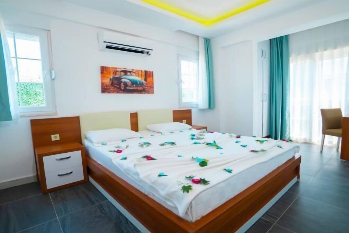 Une chambre d’hôtel avec un lit, une table de chevet, une chaise, une fenêtre et un tableau au mur.
