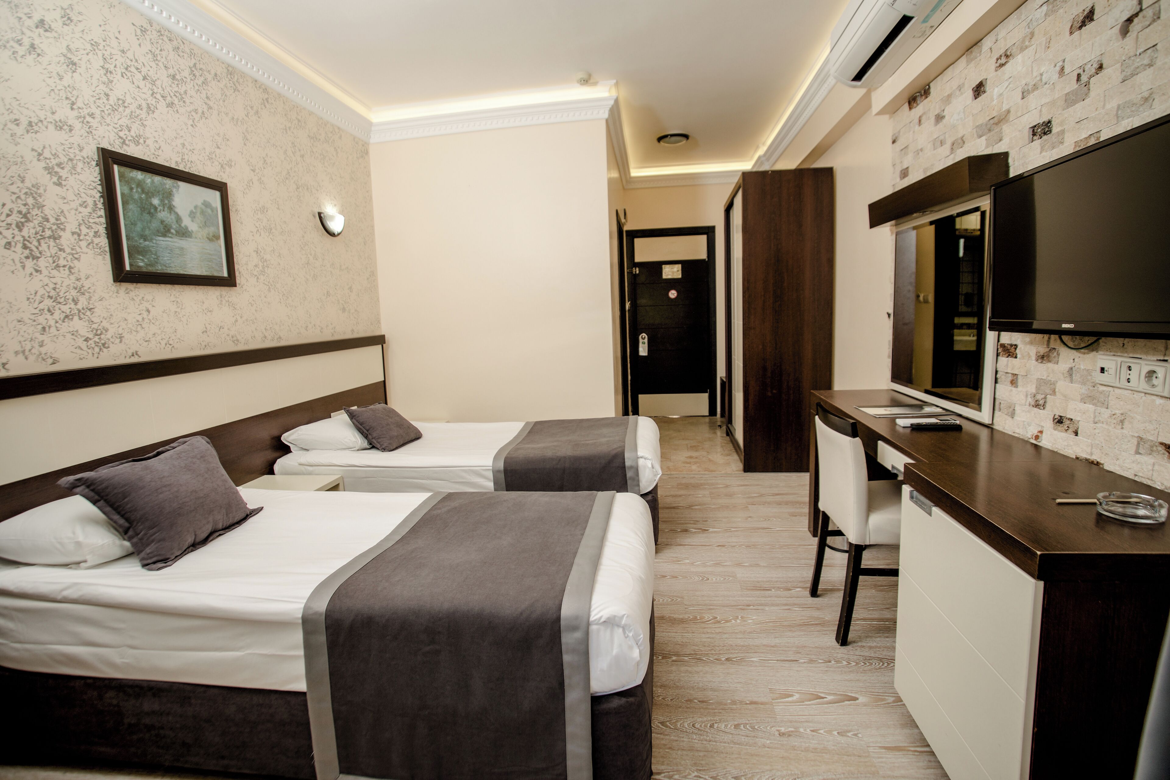 A hotel room with two beds, a desk with a television, and a bathroom visible in the background.