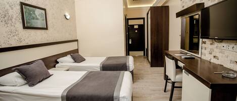A hotel room with two beds, a desk with a television, and a bathroom visible in the background.