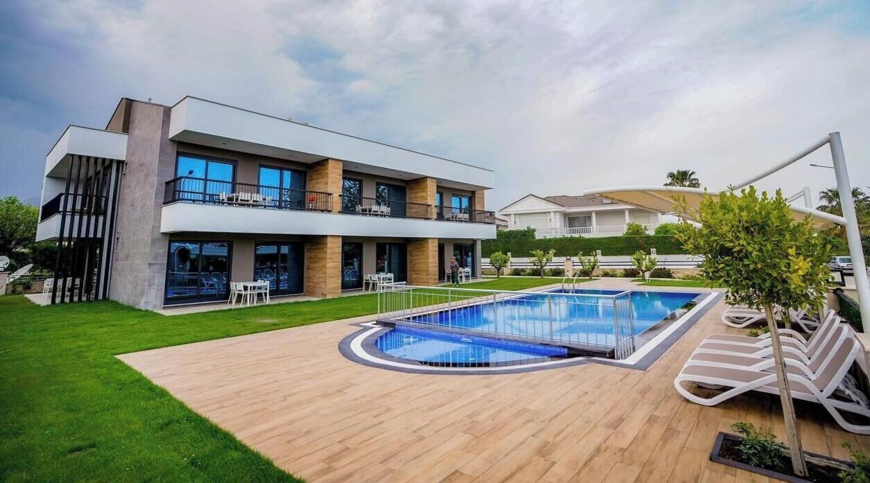 Una casa moderna de dos pisos con piscina, terraza de madera y césped cuidado.