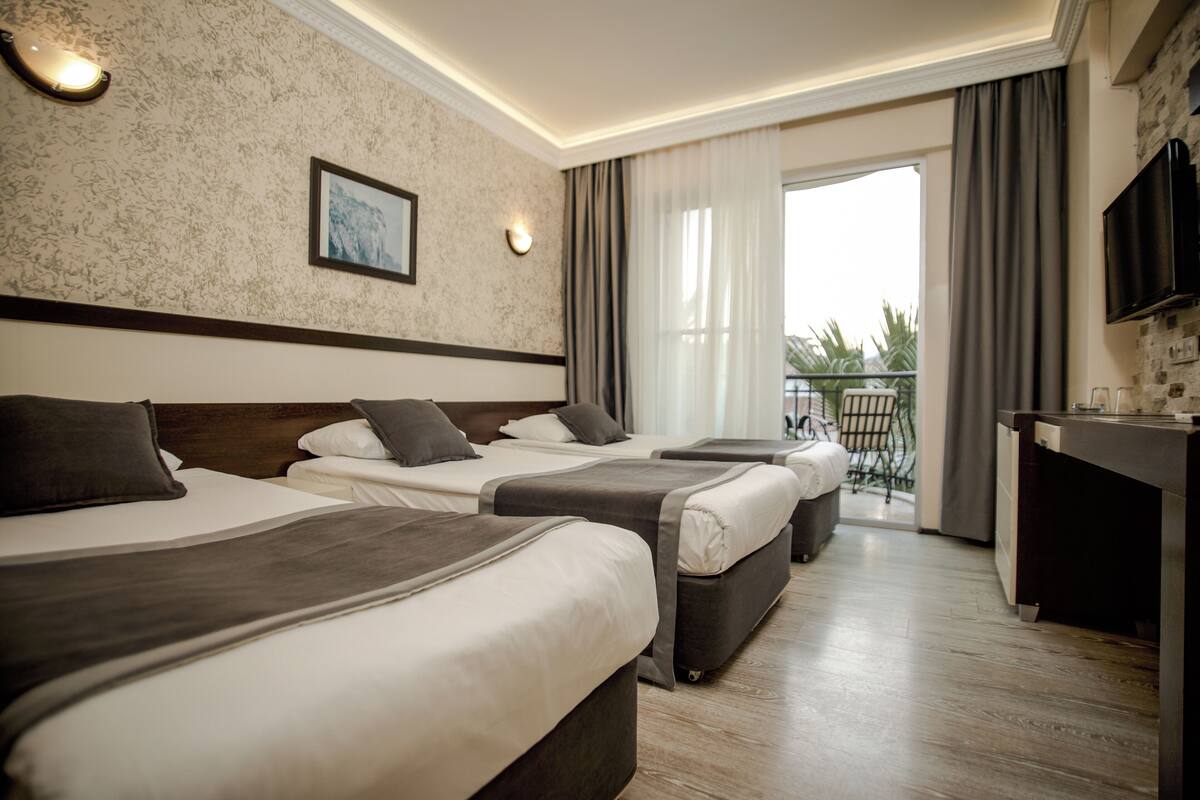 Une chambre d’hôtel avec trois lits, une télévision, un balcon avec une chaise et un plancher en bois.