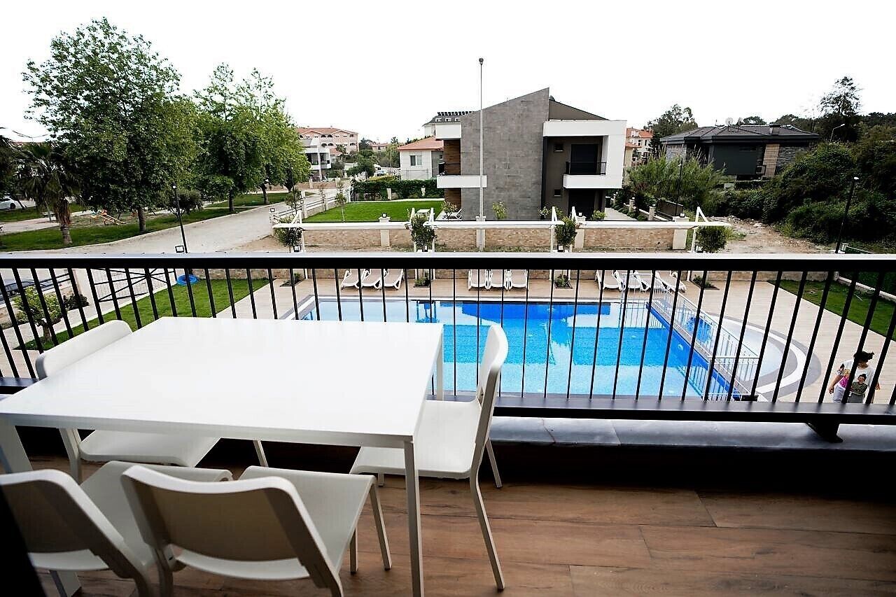 Un balcon avec une piscine, des chaises blanches et une table.
