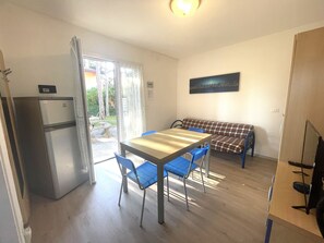 A compact kitchen with a refrigerator, a dining table with chairs, and a bench.