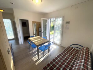 Ein Zimmer mit Holztisch, blauen Stühlen, einem karierten Bett und einer Glasschiebetür, die zu einem Außenbereich führt.