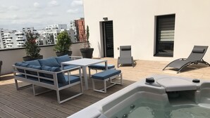 Eine Dachterrasse mit Whirlpool, einer weißen Sofagarnitur und Blumentöpfen.