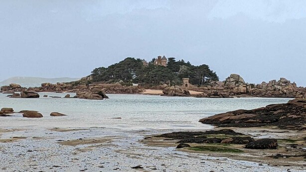 Paesaggio costiero con affioramenti rocciosi e un edificio su una collina.
