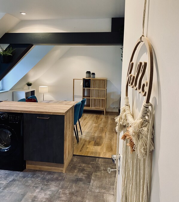 A modern kitchen with a wooden countertop, a built-in washing machine, and a staircase leading to an upper level.