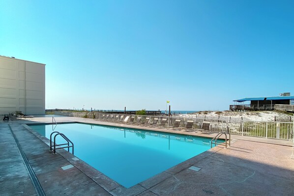 Relax by the pool surrounded by lounge chairs and umbrellas, with a wooden deck leading to a sandy area.