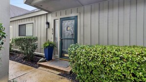 Una casa residencial con puerta principal, buzón y un pequeño jardín con arbustos y una planta en maceta.